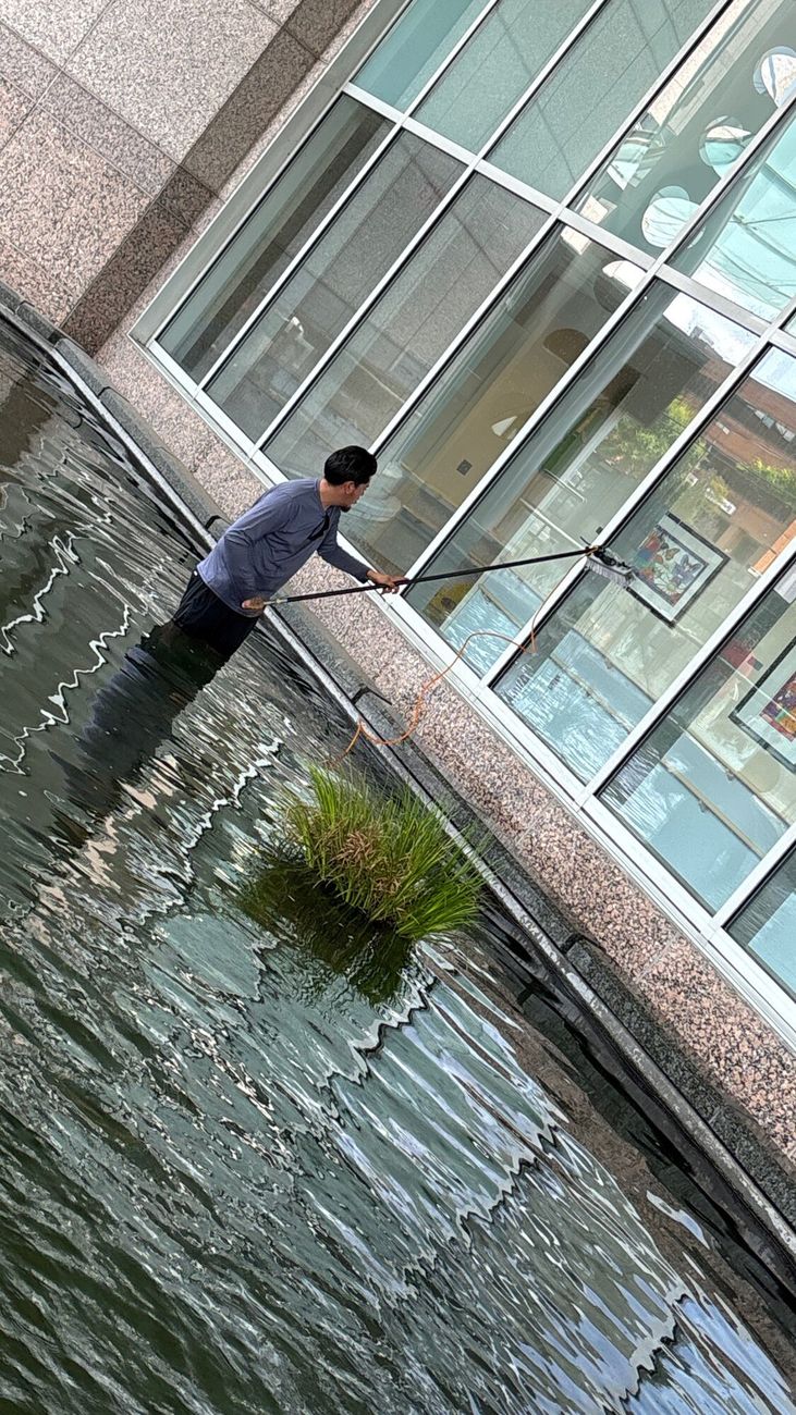 S&K technician cleaning ground-floor glass from a reflecting pool