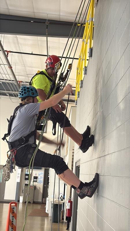 Technicians practicing rope work on an indoor training wall